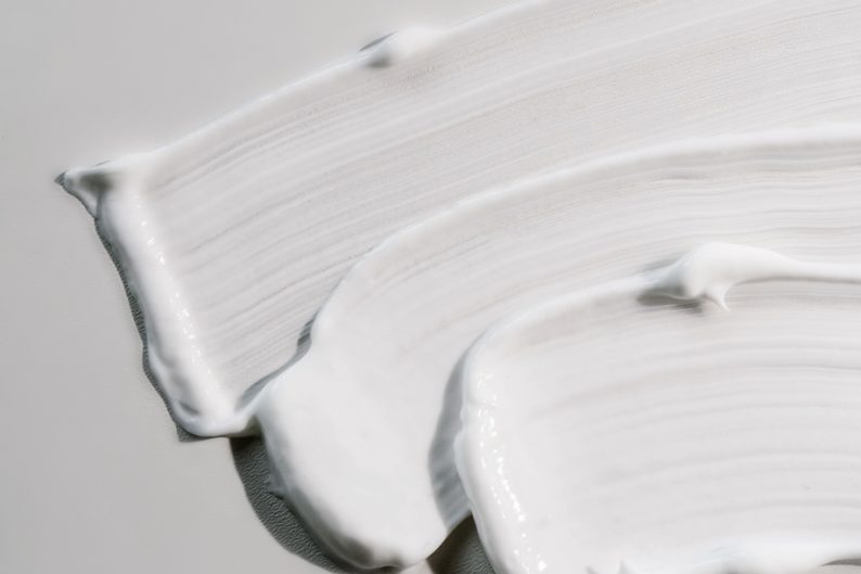 The texture of white cream on a white background on a round glass. Top view.